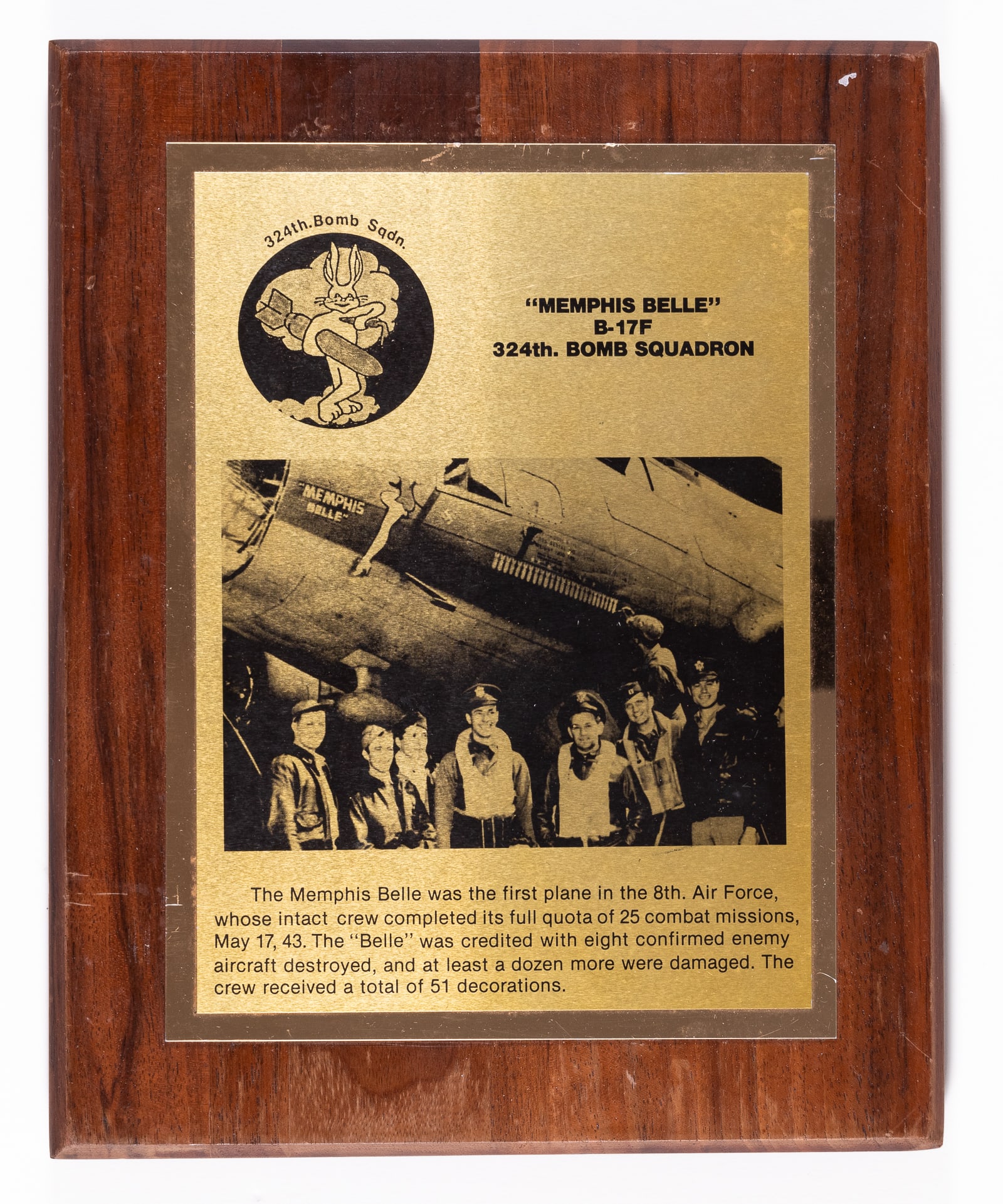 MEMPHIS BELLE COMMEMORATIVE PLAQUE: Memphis Belle 324th Bomb Squadron commemorative wood-mounted plaque. On the majority of the plaque is the patch design for the unit along with a picture of the squadron in front of the Memphis Belle. 