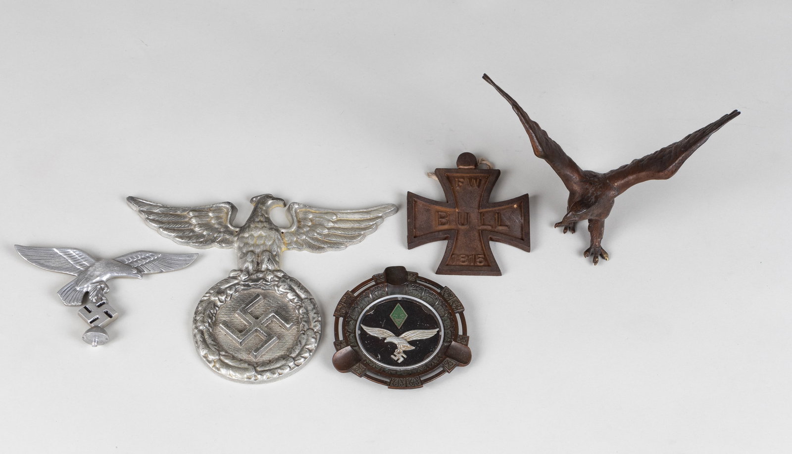 5 GERMAN METAL INSIGNIA TOPPERS: Lot of five German metal insignia wall hangers and toppers including Luftwaffe flag topper insignia, 6 x 3.75 inches; Luftwaffe insignia ashtray, 4.75 inches diameter; German eagle insignia wall hange