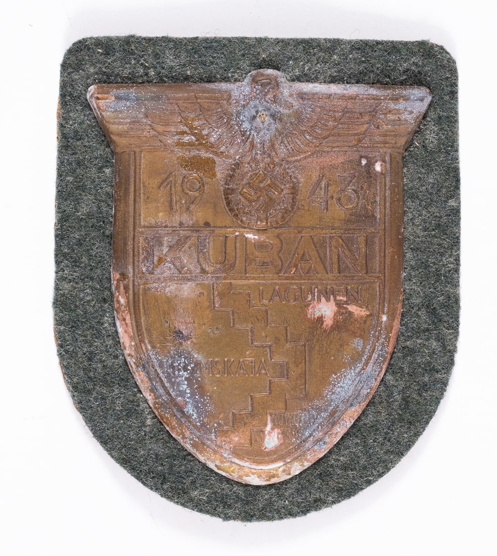 WWII GERMAN KUBAN CAMPAIGN SHIELD: WWII German Kuban campaign shield includes the Wehrmacht insignia at the top along with battle boundary lines for the Battle for the Kuban Bridgehead. Affixed to a green wool backing. 3 x 2.5 inches.