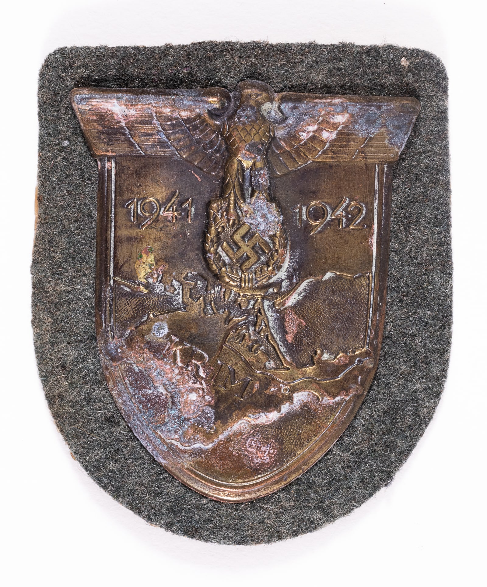 WWII GERMAN KRIM SHIELD: German Crimean (Krim) campaign uniform sleeve shield for Army troops, the reverse with intact attachment prongs connecting the shield to field-green wool. Some oxidation to the front part of the badge