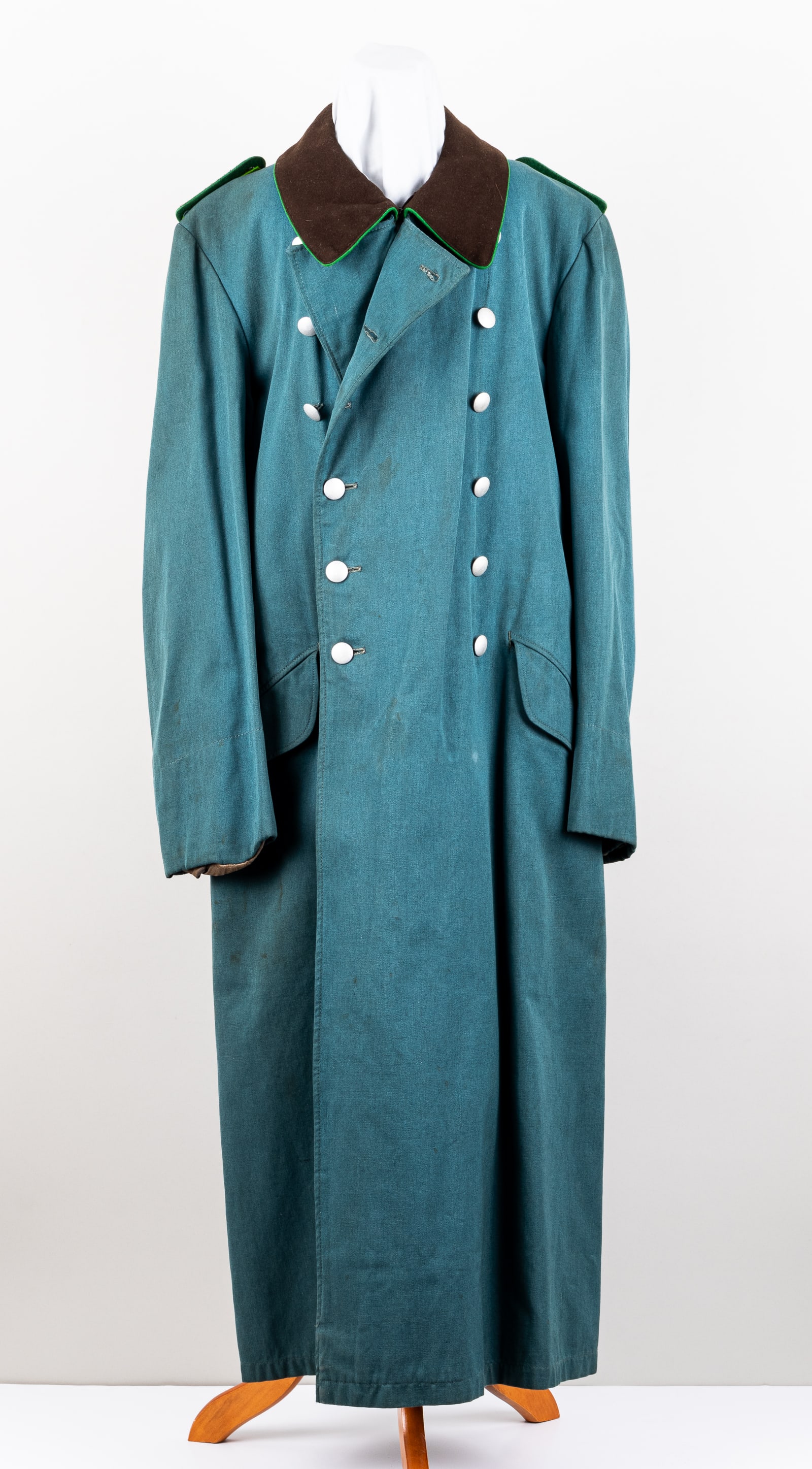 WWII GERMAN SCHUTZPOLIZEI GREAT COAT: WWII German Schutzpolizei great coat with Meister (master) shoulder boards, silver-color pebbeled buttons marked 'O.GEIGER,' 46 inches long. No rips or tears to the coat and some light staining in spo