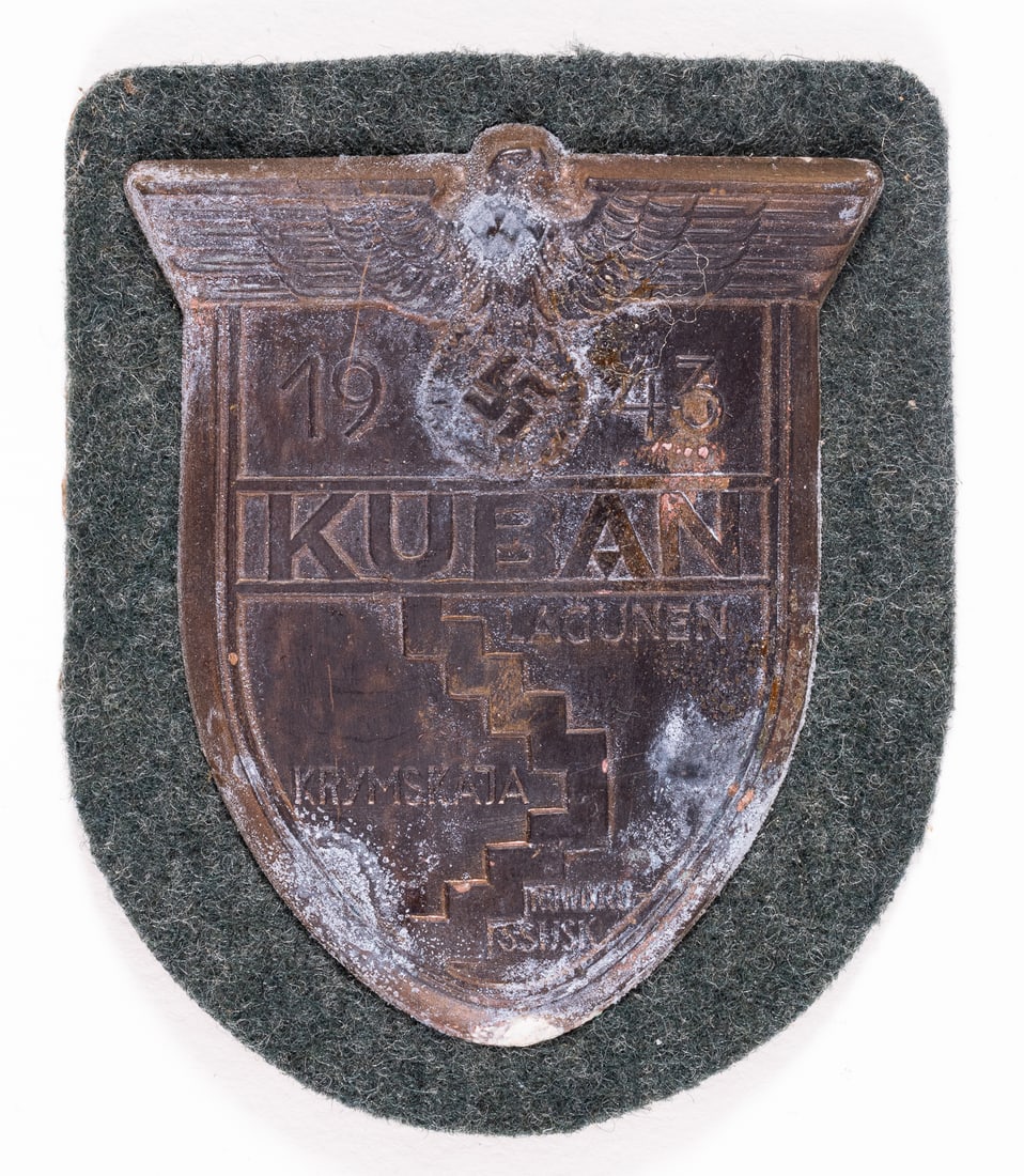 WWII GERMAN KUBAN CAMPAIGN SHIELD: WWII German Kuban campaign shield includes the Wehrmacht insignia at the top along with battle boundary lines for the Battle for the Kuban Bridgehead. Affixed to a green wool backing. 3 x 2.5 inches.