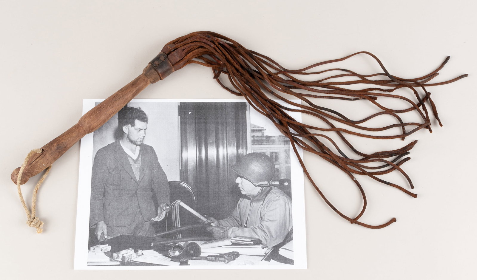CONCENTRATION CAMP GUARD WHIP: Leather whip with approx. 15-inch long tails, nailed to a 9.5-inch wooden handle, a short rope is attached to the wood handle. Makeshift whips were repurposed by guards in concentration camps for cont