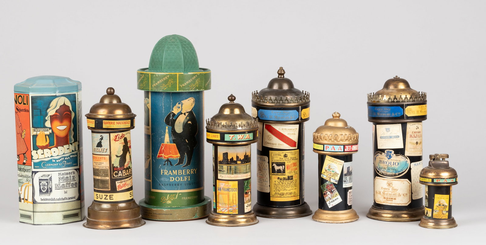 8 VINTAGE ADVERTISING PILLARS WITH FAMOUS POSTERS: Lot of eight vintage advertising pillars displaying famous posters. Including one lighter, two cigarette dispensers, two containers, a coin bank, and two music boxes. In used condition, possible dents