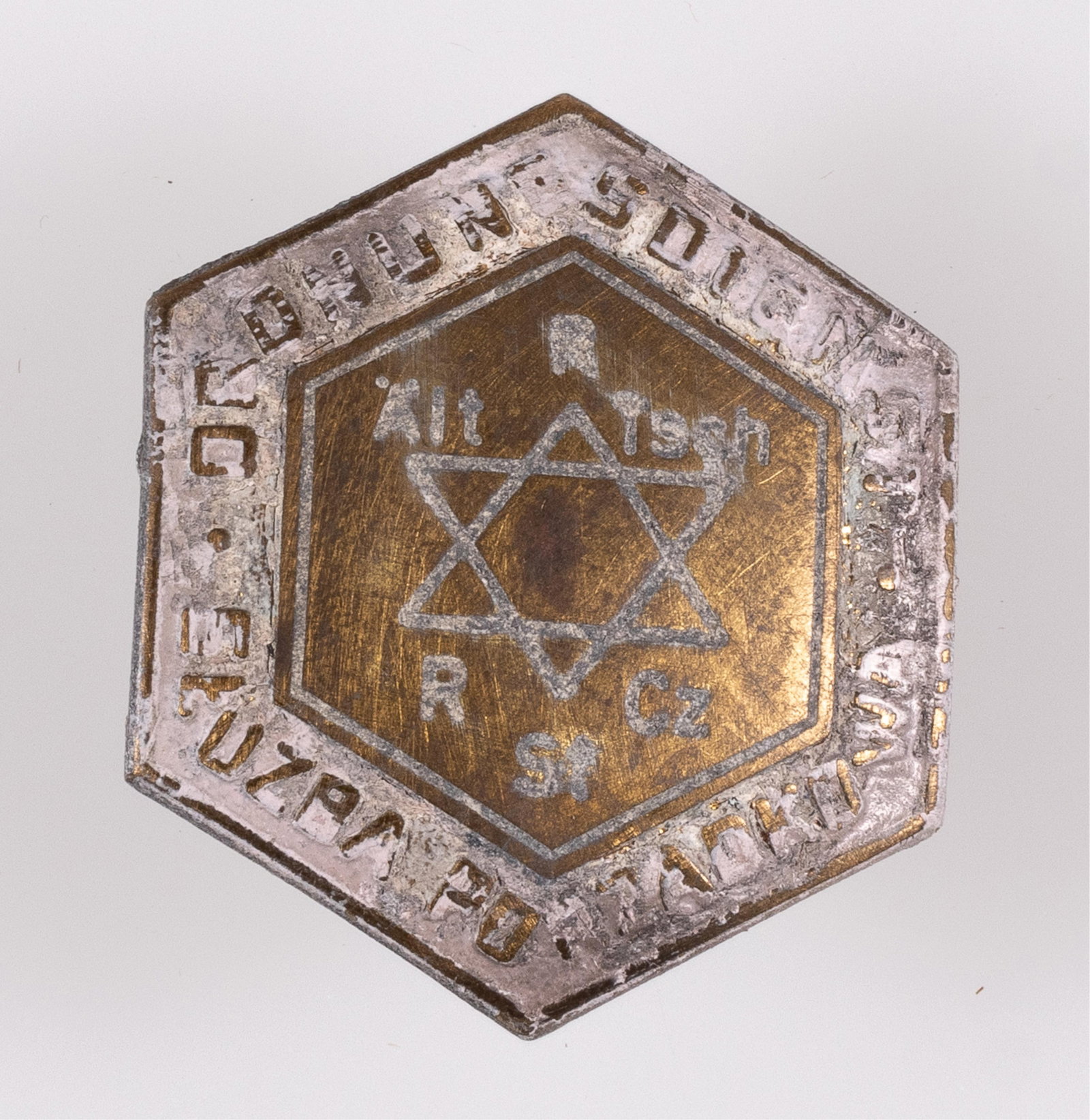 WARSAW JEWISH GHETTO POLICE CAP BADGE: Warsaw Jewish ghetto police cap badge, hexagon-shaped brass badge with a screw back mount. The badge is marked on the front 'Ordnungsdienst Sluzba Porzadkowa.' The center features a Star of David with