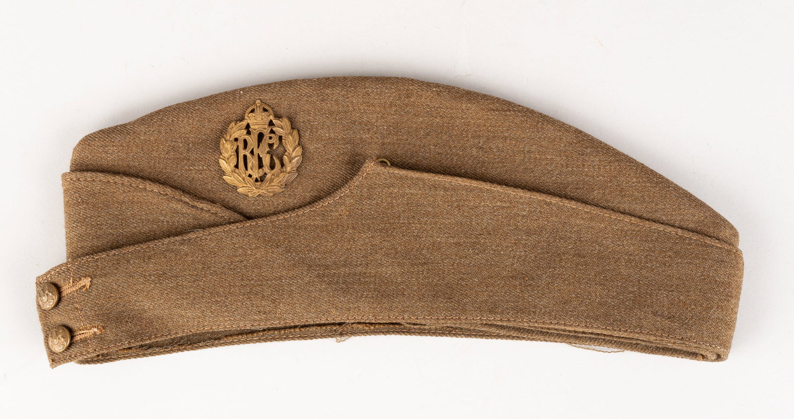 WWI BRITISH RFC OVERSEAS CAP: WWI British Royal Flying Corps overseas cap, tan color with RFC cap badge affixed to the left side of the cap. Maker information is stamped on the inside of the hat, however, it has faded to where it 