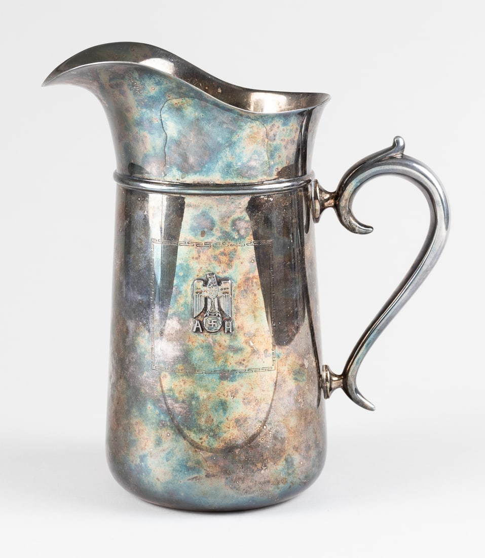 ADOLF HITLER SILVER SERVING PITCHER: Adolf Hitler silver serving pitcher, one side is decorated with the Reichseagle flanked by Hitler's initials 'AH' surrounded by a Roman Key pattern. Maker marked on the underside '800 Bruckman.' 10 in