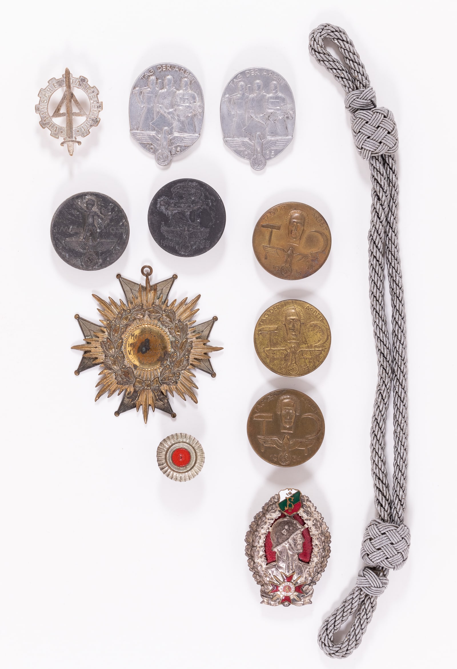 12 THIRD REICH TINNIES BADGES AND INSIGNIA: Twelve Third Reich tinnies, badges, and insignia, including a Flemish Factory Guard cap badge, a Championship medallion, a visor cap chin strap, a cockade insignia, three Tag Der Arbeit 1934 tinnies, 