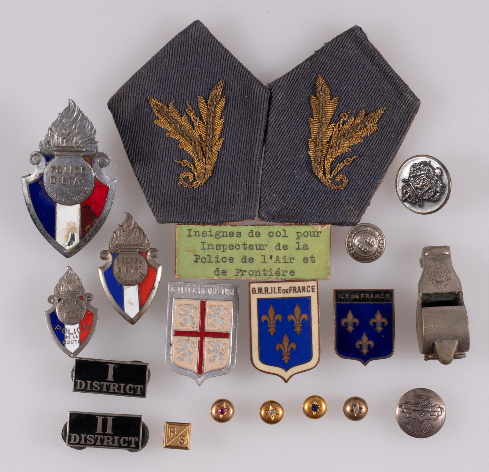 15 FRENCH POLICE D'ETAT GENDARMERIE INSIGNIA BADGES: Fifteen French police d'etat gendarmerie insignia badges, including two cap badges, a lapel pin, district collar tabs, a shirt button, a pair of collar tabs, a whistle, and three coat of arms badges.