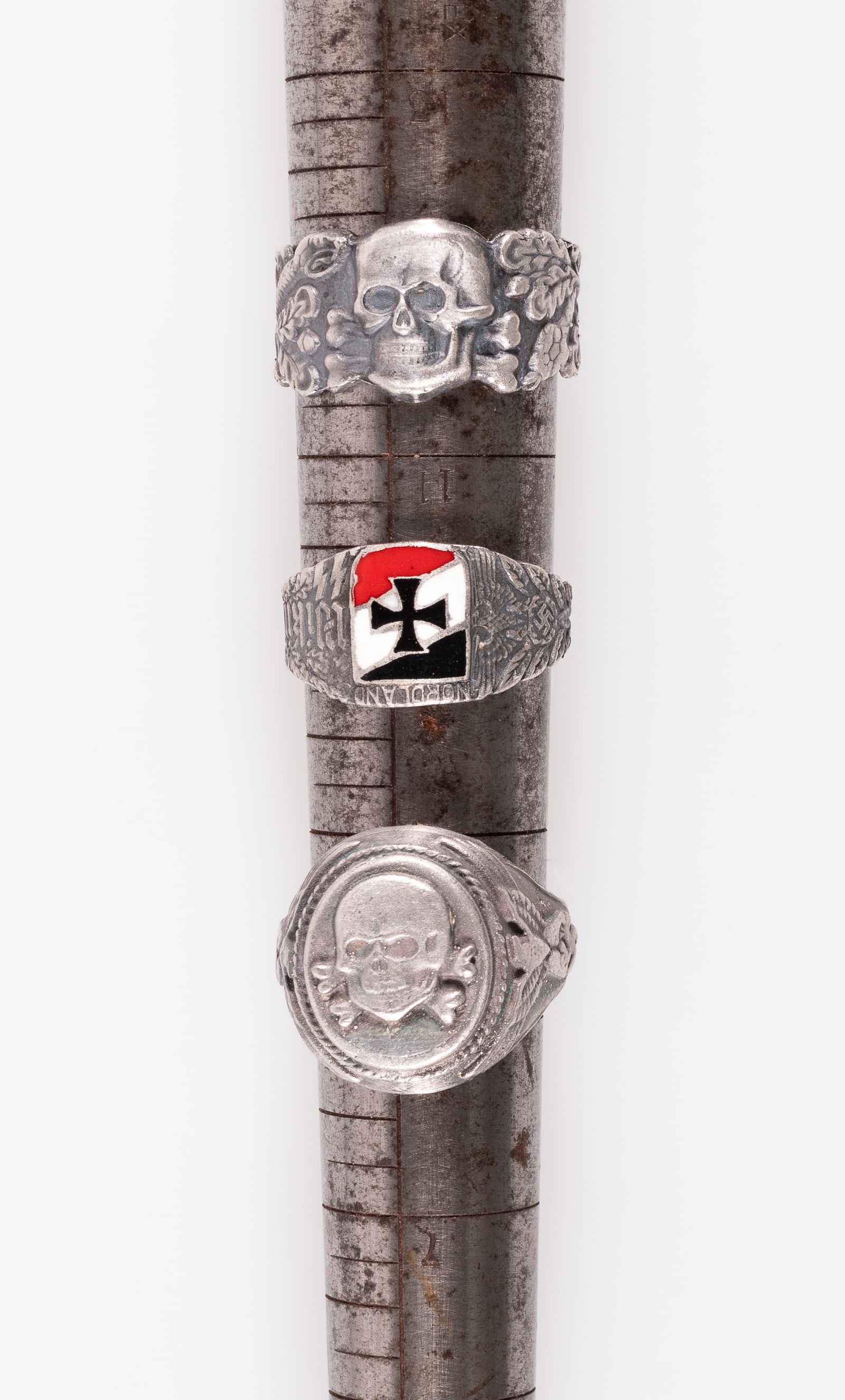 3 TOTENKOPF WAR RINGS: Two German skull and crossbones 'Totenkopf' rings, one with a skull and crossbones on the face flanked by Nazi eagles and runes, one with a skull and crossbones flanked by snakes and oak leaves, and o