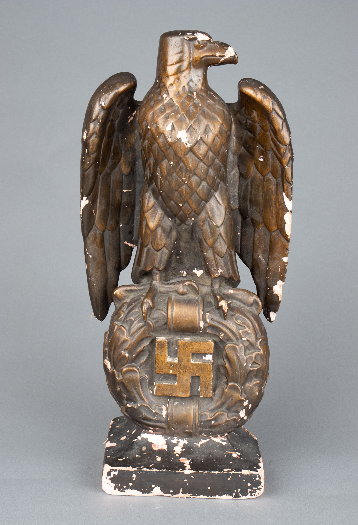THIRD REICH GERMAN REICH EAGLE STATUE: A gold-painted Third Reich German Party eagle desk statue, the eagle's talons clutch a swastika surrounded by an oak leaf wreath; its wings are folded. The statue is made of plaster and fiber construc