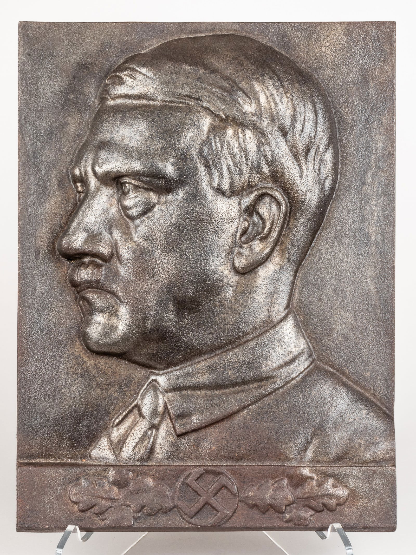 ADOLF HITLER WALL PLAQUE: Adolf Hitler heavy wall plaque, magnetic iron construction, features the face of Hitler over oak branches with a swastika in the center of them on the front, marked on the reverse '4.' 11 x 14.75 inch