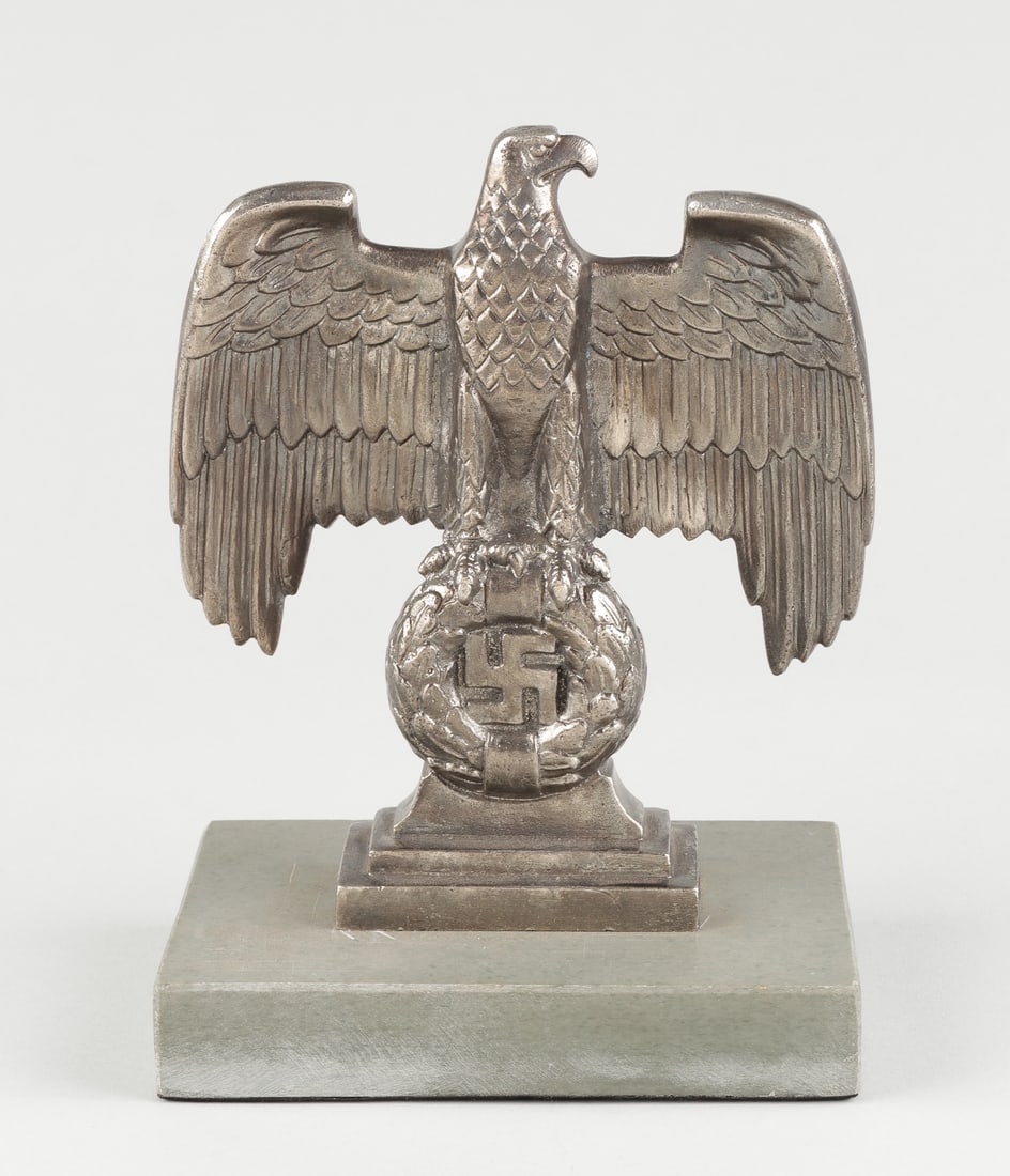 NUREMBERG NAZI DESK EAGLE: Nuremberg Nazi desk eagle with spread wings sitting on top of a large oak leaf wreath with a static swastika in the center. Marked with 'RZM M3/90' on the verso of the statue, and is mounted to a slat