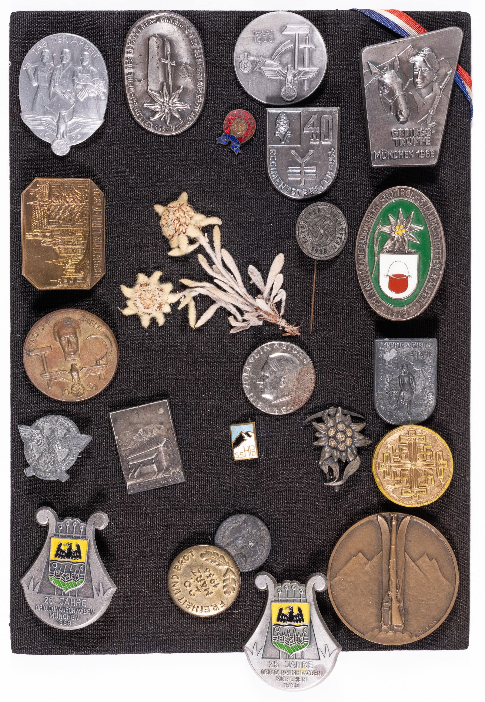 GERMAN WWII TINNIES DISPLAY: Lot of seventeen German WWII tinnies, including two edelweiss tinnies, and edelweiss dried flower, an Adolf Hitler tinnie, Tag der Arbeit tinnies, and more. Also includes five post-war tinnies, mostly