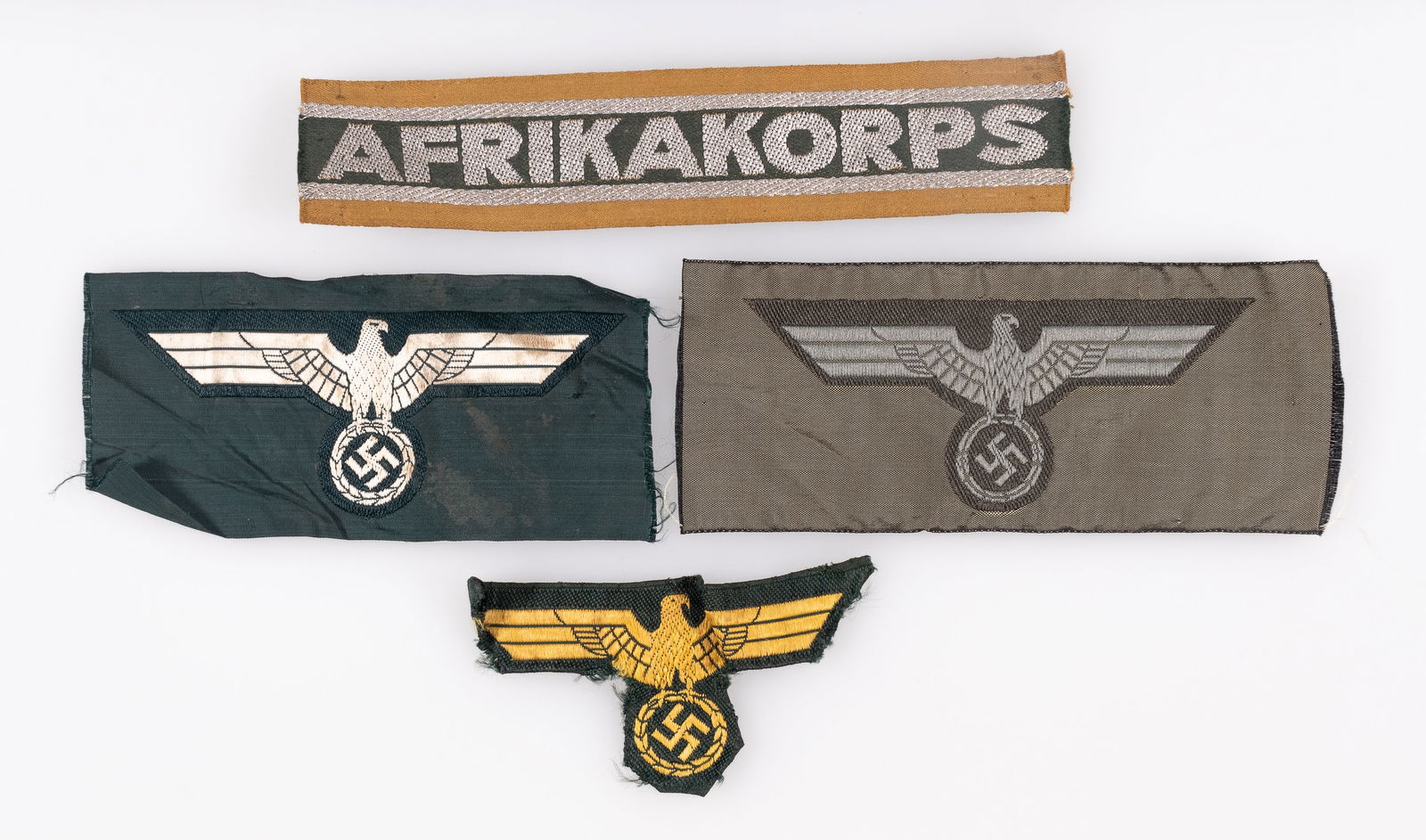 4 WWII GERMAN INSIGNIA PATCHES: Four WWII German insignia patches, including an Afrikakorps cuff title, trimmed, 6.25 inches long, a Heer Eagle cap badge, a Kriegsmarine Coastal Artillery breast eagle, a Heer M36 breast eagle, and a
