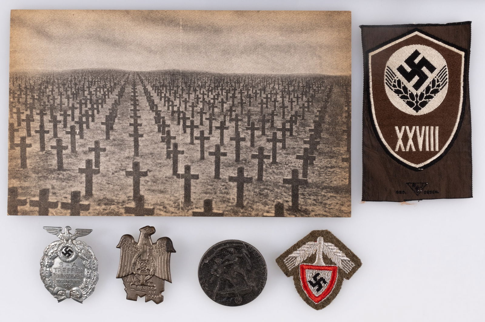 5 WWII GERMAN PINS AND INSIGNIA: Five WWII German Pins and insignia, including an SA Treffen Braunschweig 1931 tinnie, an NSKV tinnie from a 1935 Saar Reunification event, a 1938 Reichsparteitag tinnie, an RAD cloth cap insignia patc