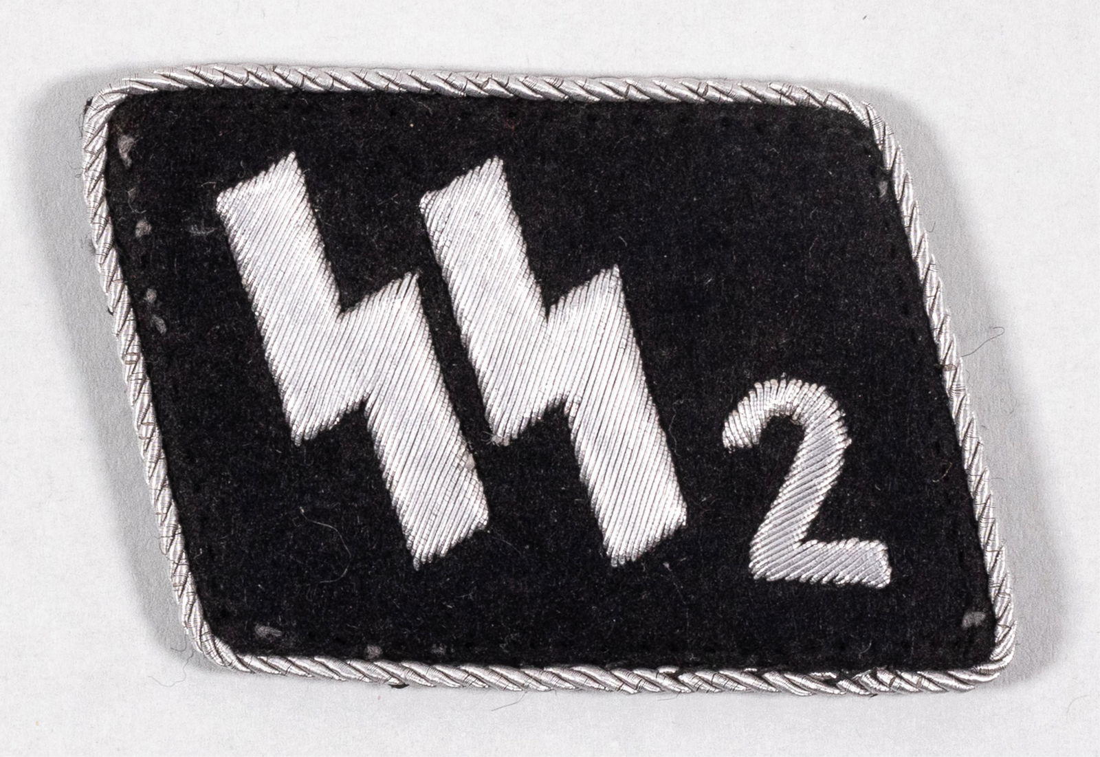 WAFFEN-SS STANDARTE 2 GERMANIA COLLAR TAB: Waffen-SS Standarte 2 'Germania' collar tab. Black cloth, aluminum embroidered SS runes with the numeral '2'. Edged with twisted aluminum string border.