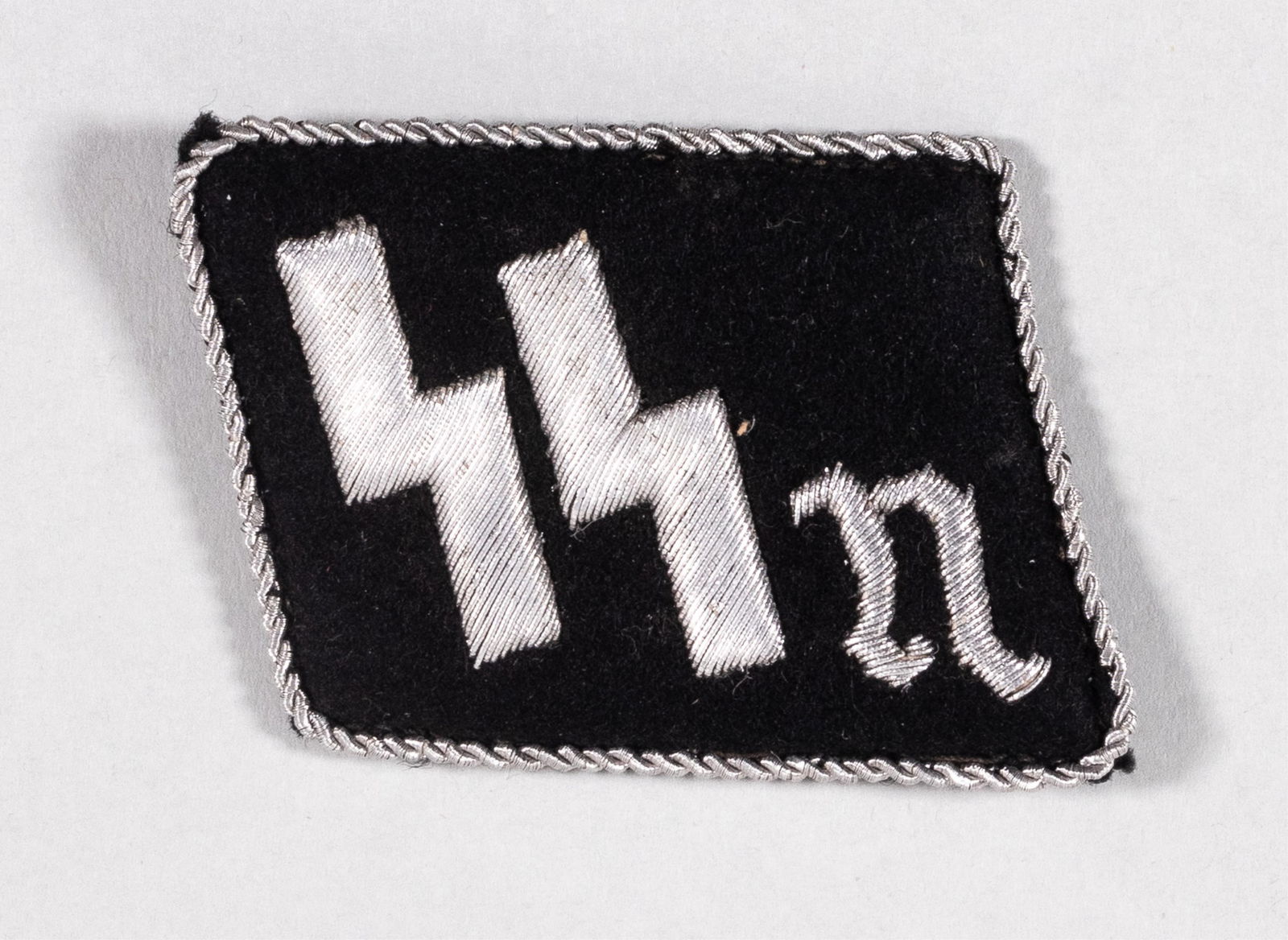 SS-VT STURMBANN NUREMBERG RIGHT COLLAR TAB: SS-VT Sturmbann Nuremberg right collar tab. Black cloth, aluminum embroidered SS runes and the letter 'N'. Edged with twisted aluminum string border. The Sturmbann Nuremberg was absorbed into the Anti