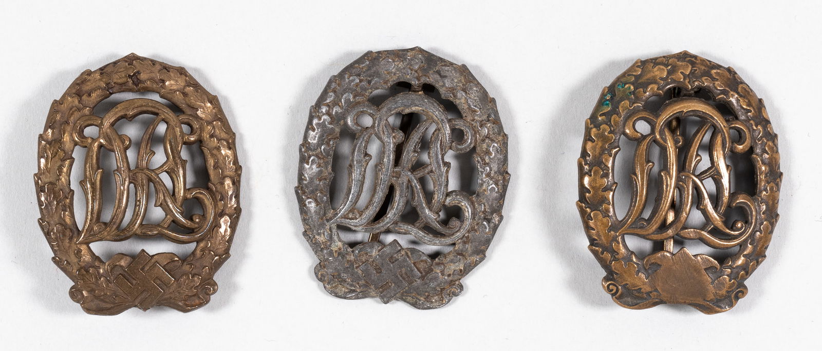 3 WWII GERMAN DRL SPORTS BADGE: A lot of three WWII DRL sports badges, two in bronze and one in silver. One bronze badge de-nazified with the swastika shaved off, one bronze badge marked on the back 'LCHR LAUER - Nurnberg-Berlin - D