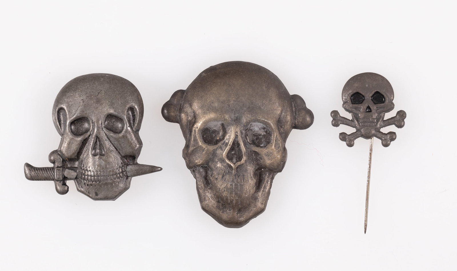 3 WWII ITALIAN TOTENKOPF CAP BADGES: Three WWII Italian Totenkopf badges, including an Arditi RSI Black Shirts Elite cap badge, centerpin back, a cap badge with the bottom bones missing, safety pin style backing, and a stickpin.