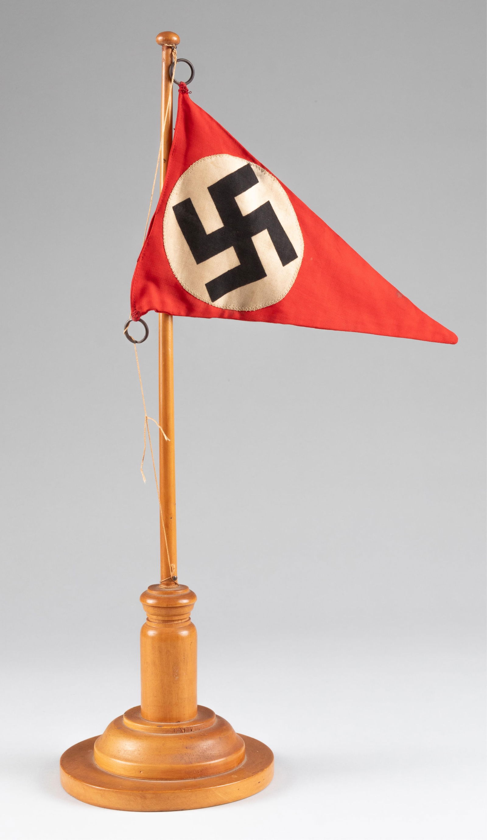 WWII NSDAP DESK PENNANT AND FLAGPOLE: WWII NSDAP desk pennant and flagpole. Double-sided pennant, red background with white disks with black swastikas in the center. Two metal rings are attached to the corners to hang on the flagpole, wit