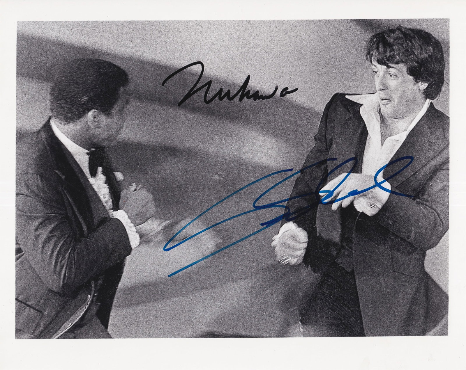 MUHAMMAD ALI & SYLVESTER STALLONE: Black-and-white photograph of Muhammad Ali and Sylvester Stallone play-fighting at the 1977 Academy Awards ceremony, where the movie Rocky won the Oscar for best picture. Signed at the top in black in