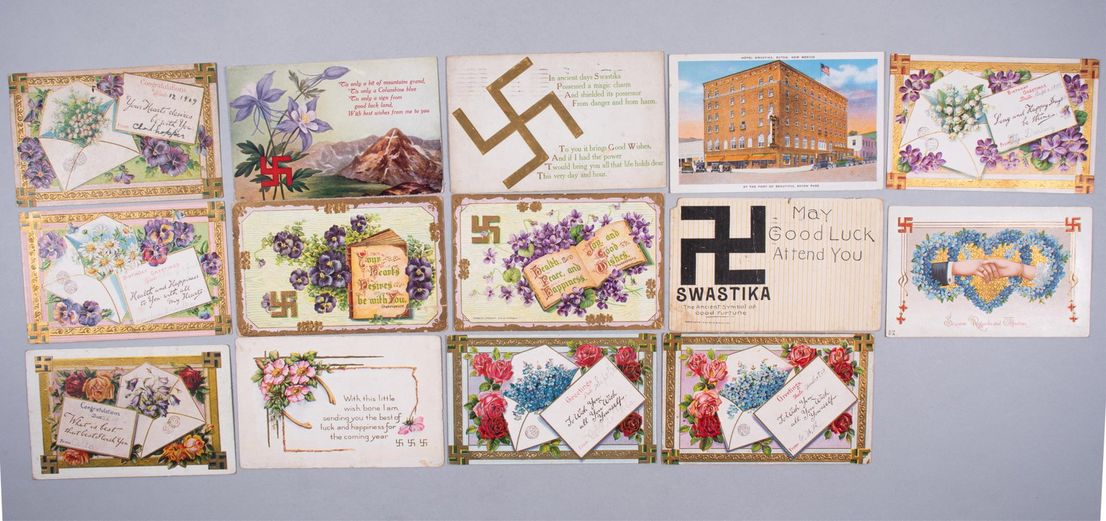 14 AMERICAN SWASTIKA GOOD FORTUNE POSTCARDS: Fourteen American postcards with swastika motifs, dated from 1909 to 1910. Seven are postally used, with inscriptions on the verso. One postcard features the Hotel Swastika, once a fancy brick buildin