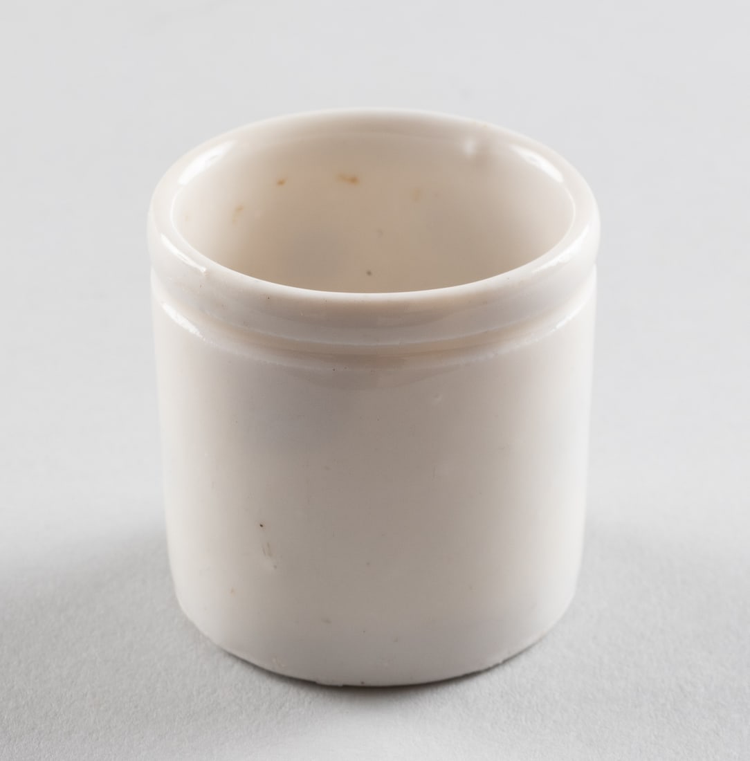 KL AUSCHWITZ BUNA WERK CERAMIC MEDICAL CUP: Ceramic cup for medical samples from the concentration camp KL Auschwitz, stamped on the bottom 'SS Arbeitsamt Buna Werke KL Auschwitz 551.' 1 3/4 x 1 3/4 in.