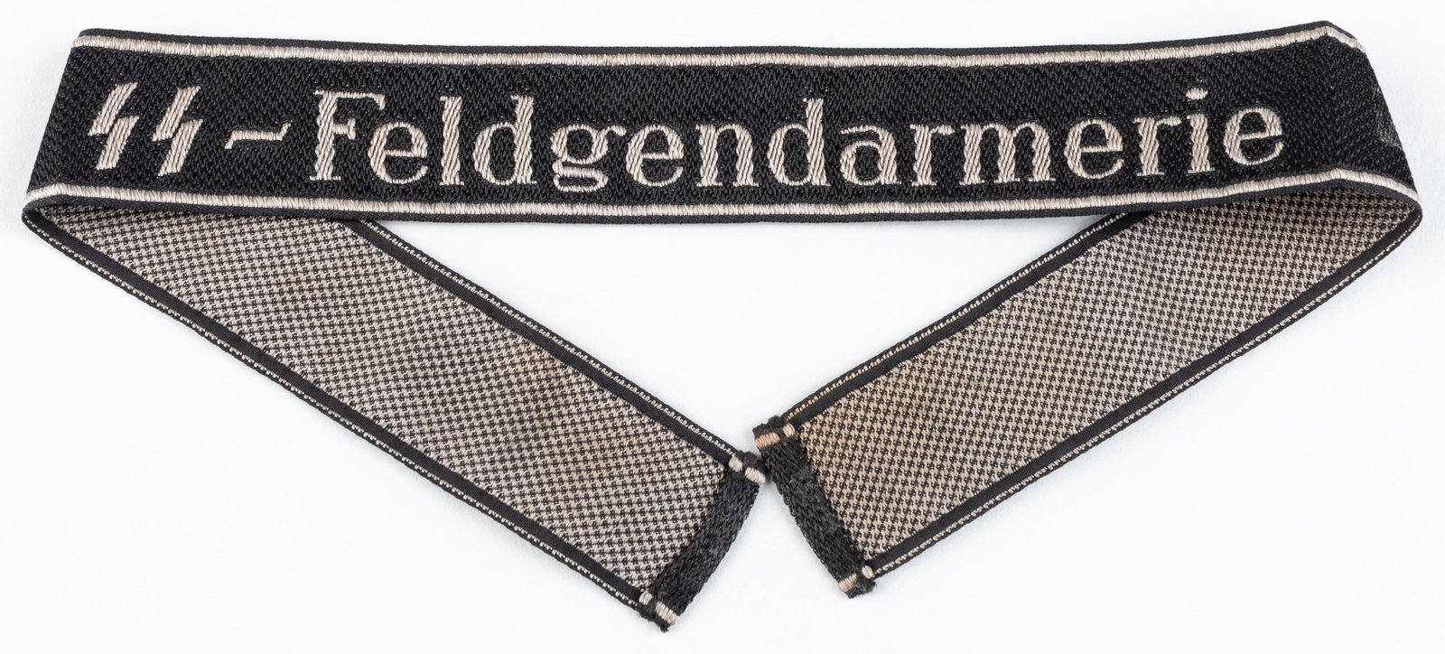 SS-FELDGENDARMERIE ENLISTED CUFF TITLE: WWII SS-Feldgendarmerie enlisted cuff title, BeVo style stitching with silver/gray lettering and silver/gray borders at the top and bottom margins, reads 'SS-Feldgendarmerie' in the center in Latin sc