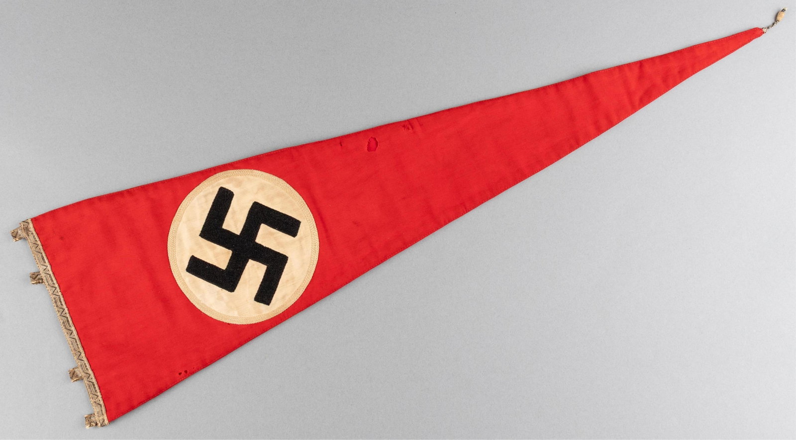 EMBROIDERED NSDAP NAZI PARTY PENNANT: Large ornate embroidered double-sided NSDAP party pennant, tassel at the point, and a Roman key brocade with hanging loops at the hoist. Embroidered swastika on a white circle. Small moth nips, stain