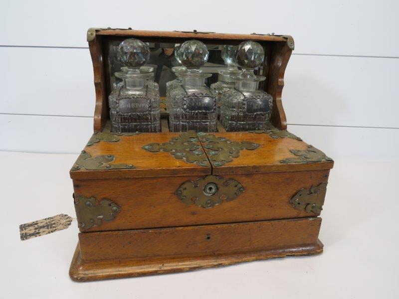 English Oak Tantalus Liquor Cabinet: Decanters have the silver-plated hanging labels for Bourbon - Scotch - Rye. Missing the glasses. Showing some nicks to the wood along the base and missing some of the nails to the brass ornamenta