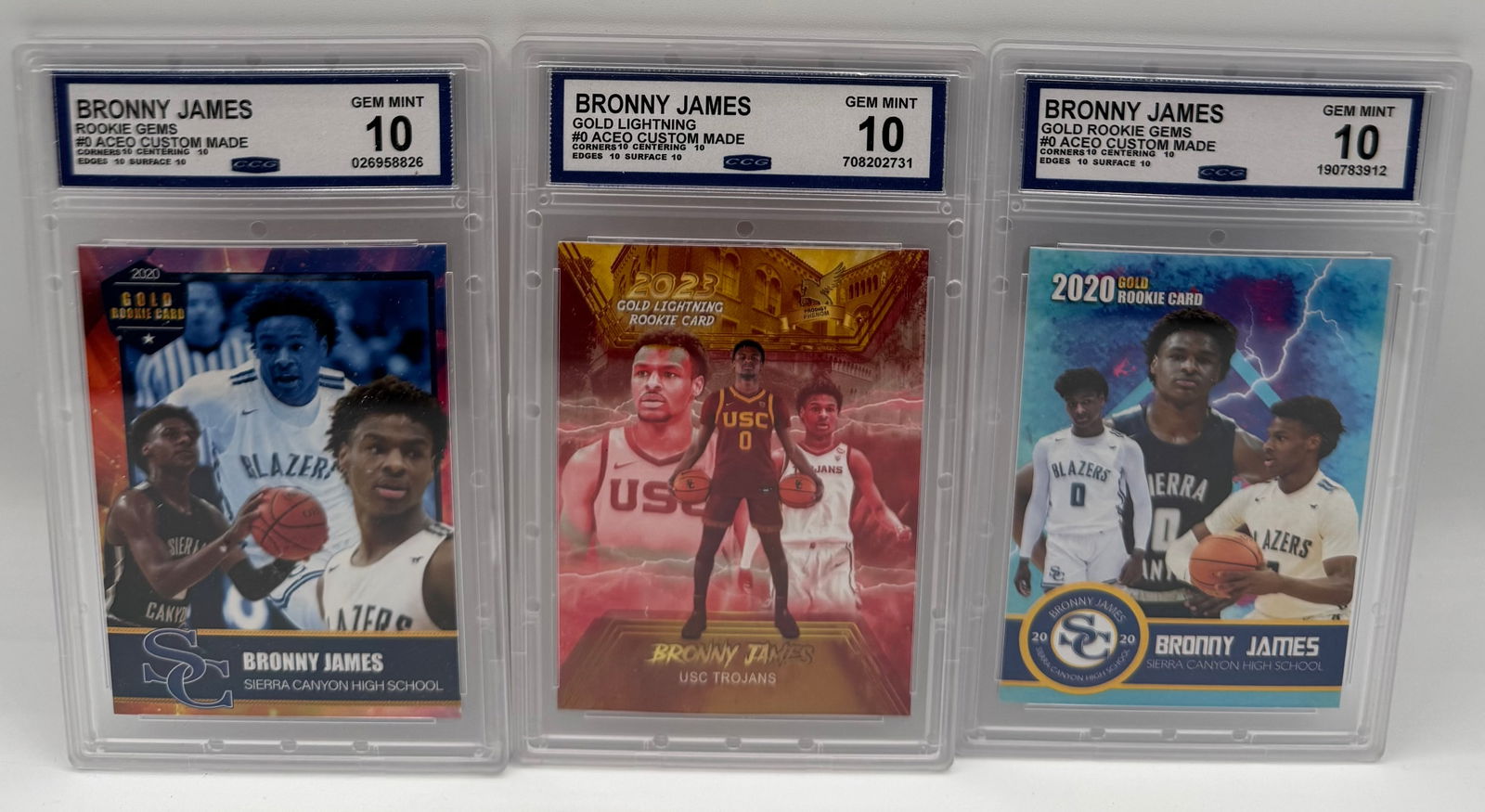 (3) Bronny James ACEO Custom Rookie Cards - Sierra Canyon & USC - Gem Mint 10: Card 1: 2020 Rookie Gems #0 ACEO Custom (Sierra Canyon). Graded Gem Mint 10 by CCG. • Card 2: 2023 Gold Lightning #0 ACEO Custom (USC Trojans). Graded Gem Mint 10 by CCG. • Card 3: 2020 Go
