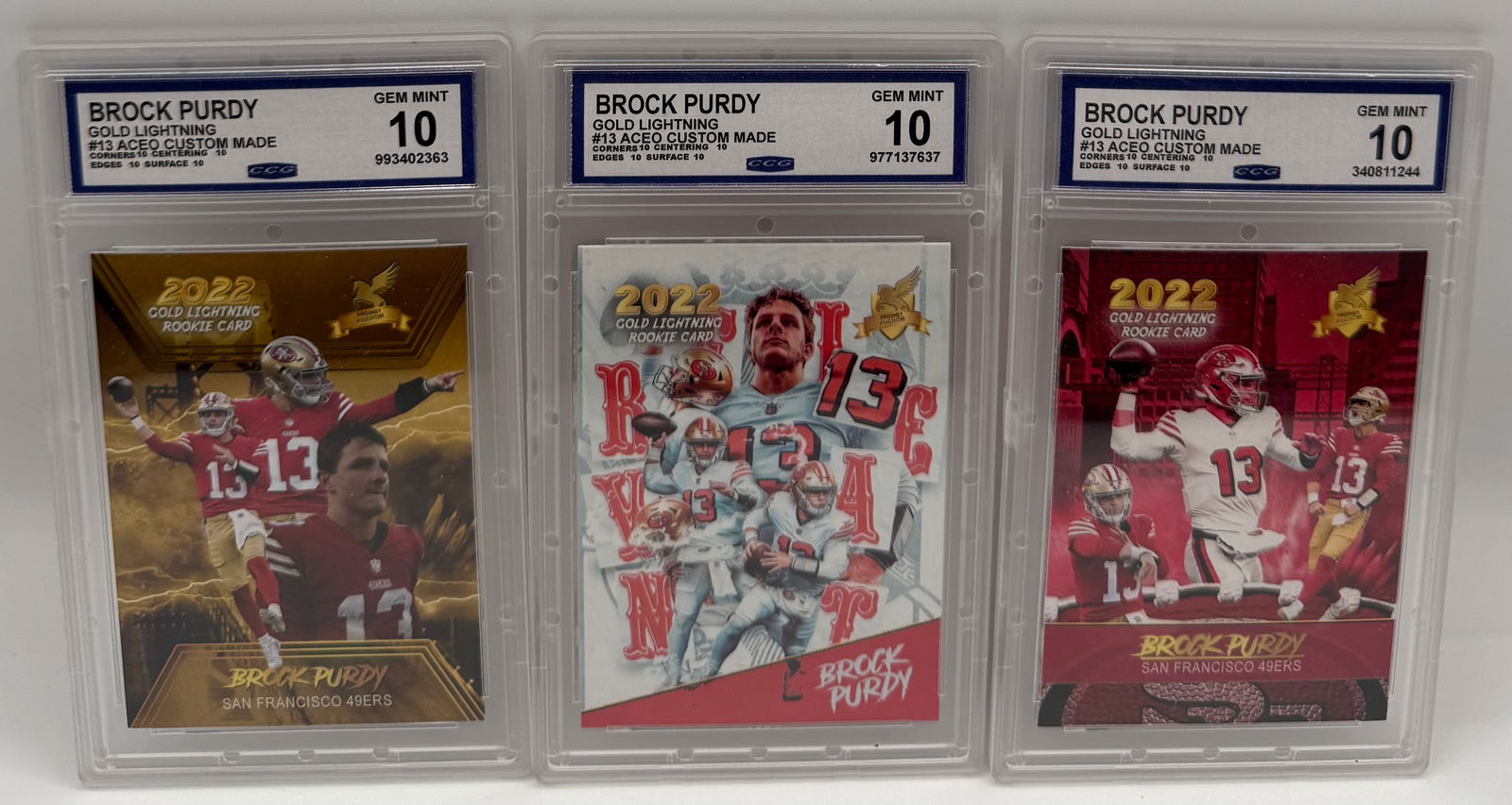 (3) 2022 Brock Purdy ACEO Custom Rookie Cards - Gold Lightning Series - Gem Mint 10: A trio of Brock Purdy custom-made "Gold Lightning" rookie cards. • Details: All three cards are graded Gem Mint 10 by CCG. • Features different artistic backgrounds including the "Red