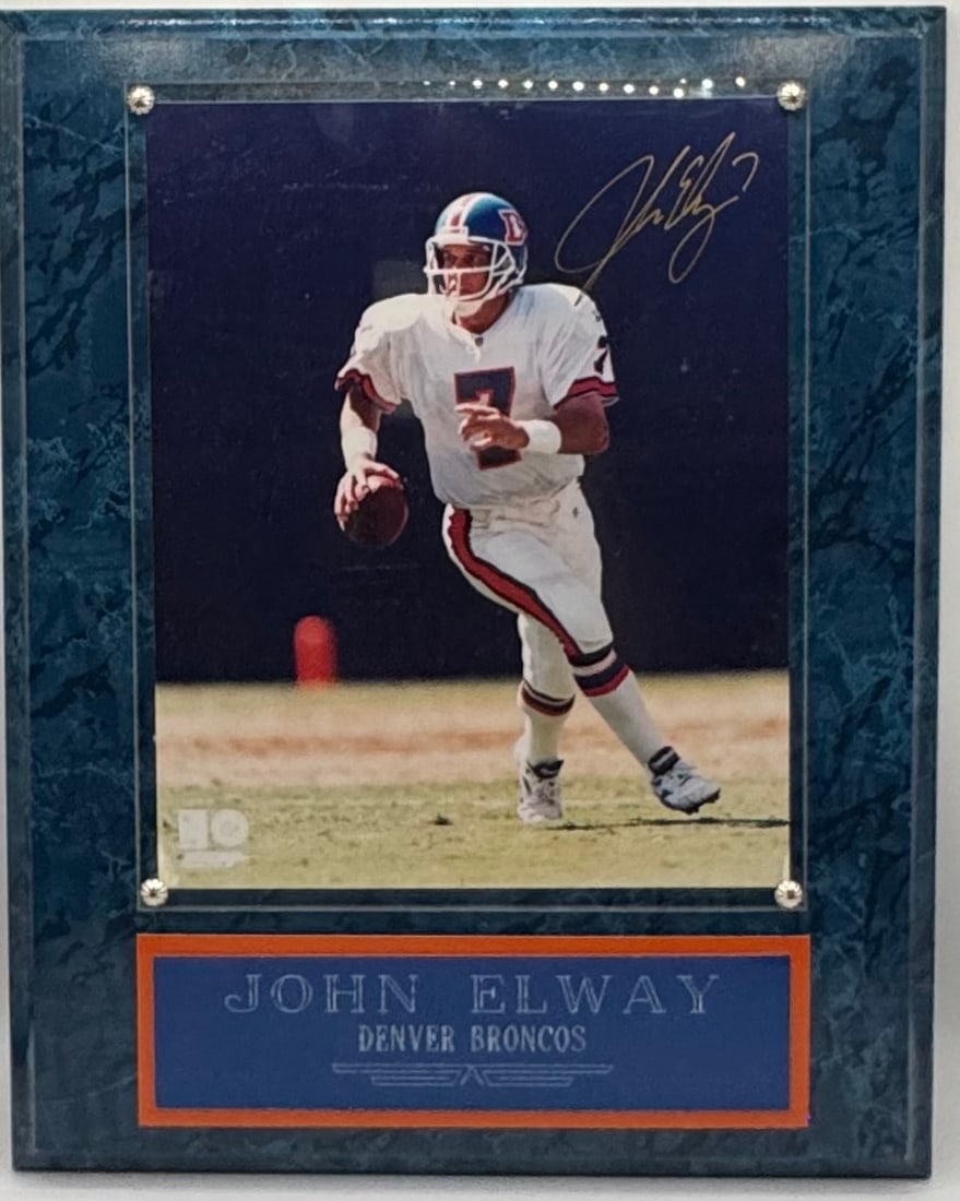 John Elway Signed Denver Broncos Action Photo with COA: An authentic hand-signed 8x10 color photograph of Hall of Fame quarterback John Elway in his classic Denver Broncos home uniform. The piece is professionally mounted on a blue marble-finish wood