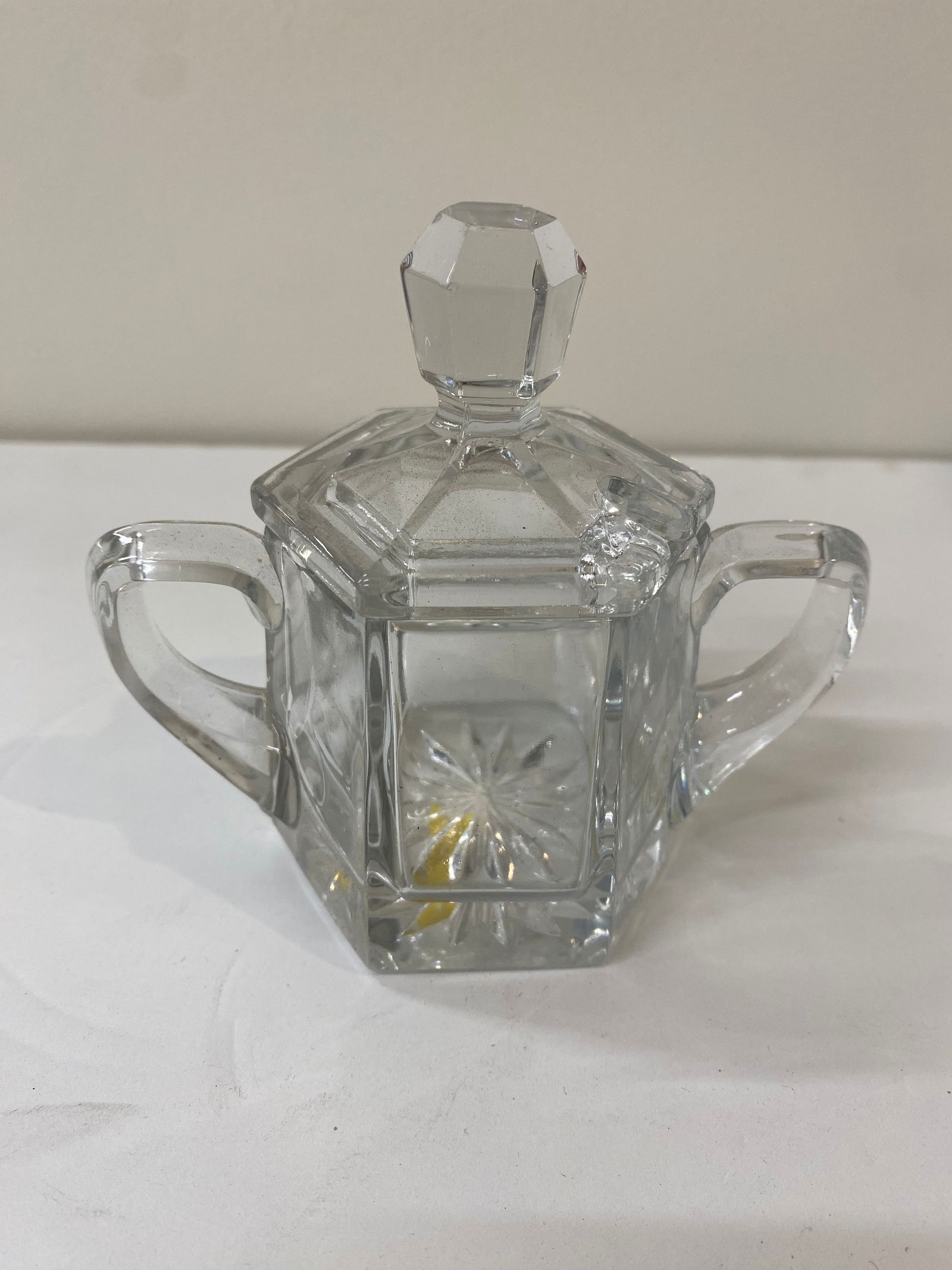 Art Deco Style Pressed Glass Sugar Bowl: A clear pressed glass sugar bowl featuring a geometric octagonal shape and dual handles. The lid is topped with a faceted finial, and the base features a classic starburst/sunburst pattern. •
