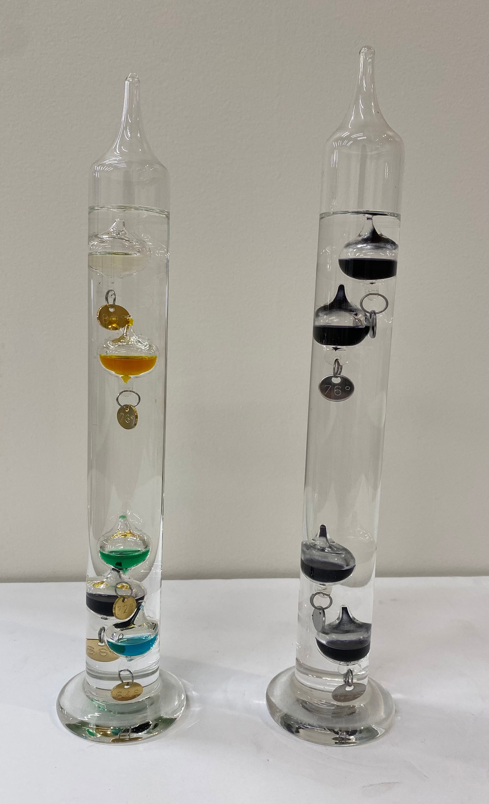 Pair of Galileo Glass Thermometers - Colorful & Monochrome Floating Spheres: A stunning pair of hand-blown art glass champagne flutes. Features a flared amber bowl with a lustrous iridescent finish, transitioning into a deeply ribbed cobalt blue stem and base. •