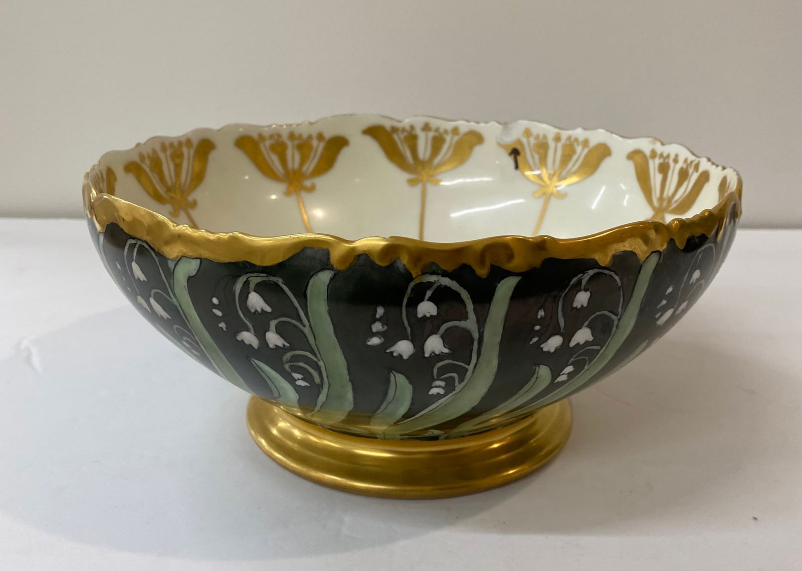 Fine Hand-Painted Porcelain Pedestal Bowl - Lily of the Valley & Gold: An exquisite footed porcelain bowl featuring a dramatic black exterior decorated with delicate "Lily of the Valley" floral sprays. The interior is finished in white with stylized gold floral motifs. H