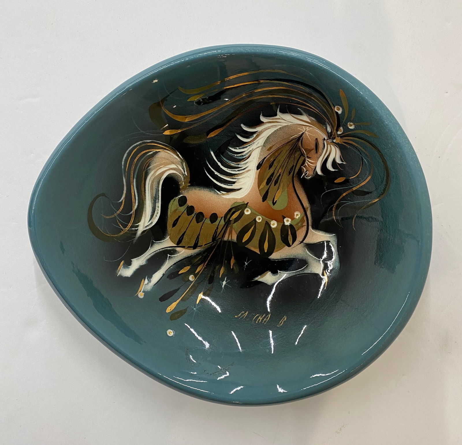 Sascha Brastoff Signed Mid-Century Modern Ceramic Dish – Horse Motif: A free-form ceramic tray in a teal-blue matte finish, hand-painted with a stylized "Star Steed" or prancing horse in gold and earth tones. Signed "Sascha B." on the front. A prime example of 1950s