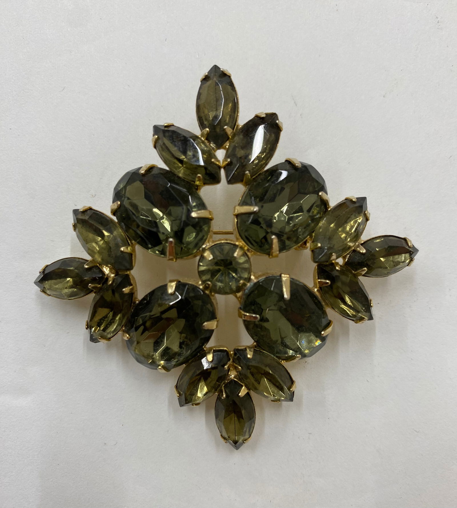 Vintage Mid-Century Gilt Metal & Smokey Quartz Rhinestone Brooch: A statement costume jewelry brooch in a tiered floral/starburst arrangement. Set with large oval and marquise-cut "Smokey Quartz" colored glass rhinestones in a gold-tone claw setting. Secure pin