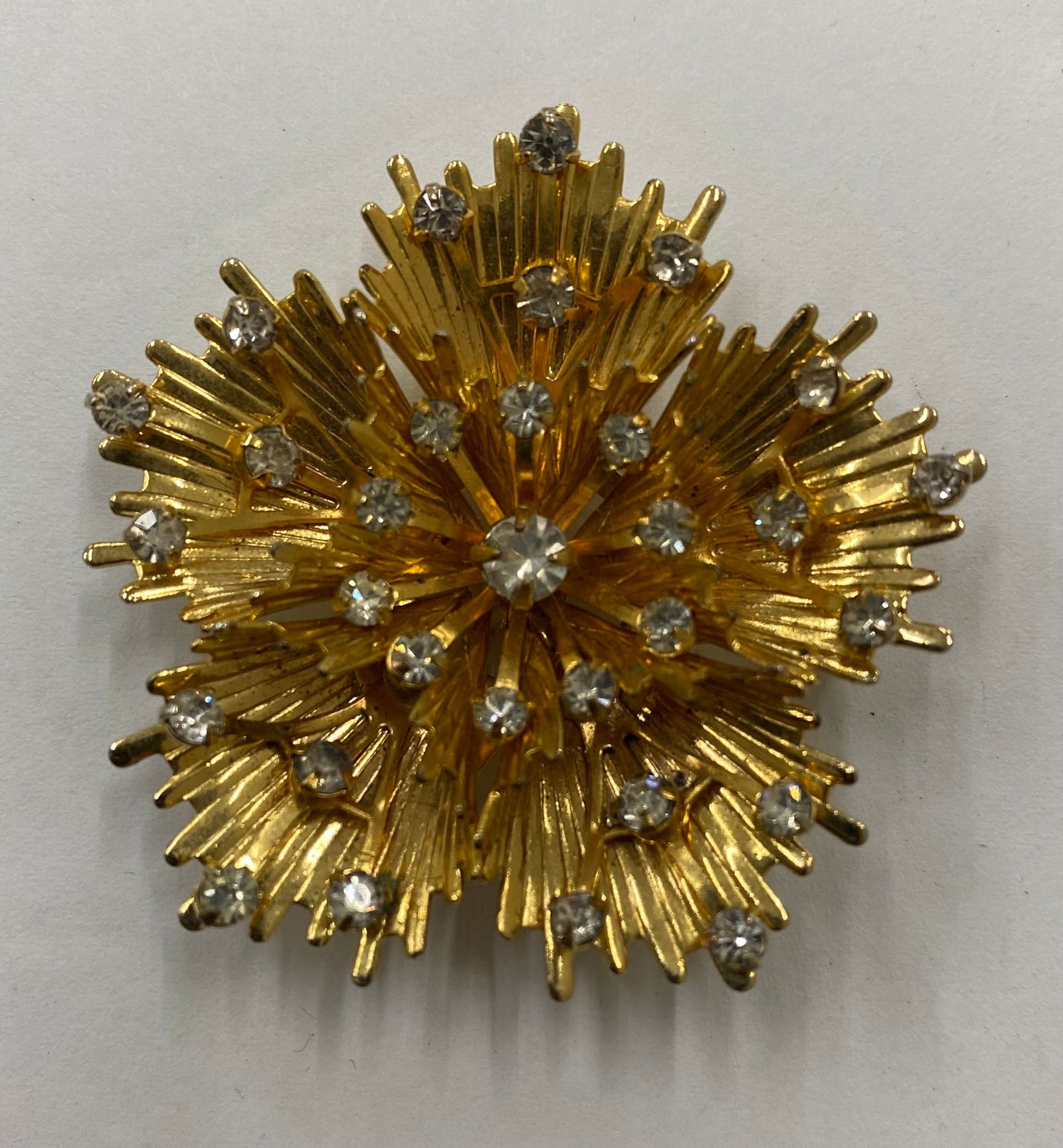 Vintage 1960s Gold-Tone Sunburst Brooch with Clear Rhinestones: An elegant "spiked" sunburst or floral motif brooch in a bright gold-tone finish. The layered, textured petals are accented with tiered clear round-cut rhinestones, creating a high-dimension