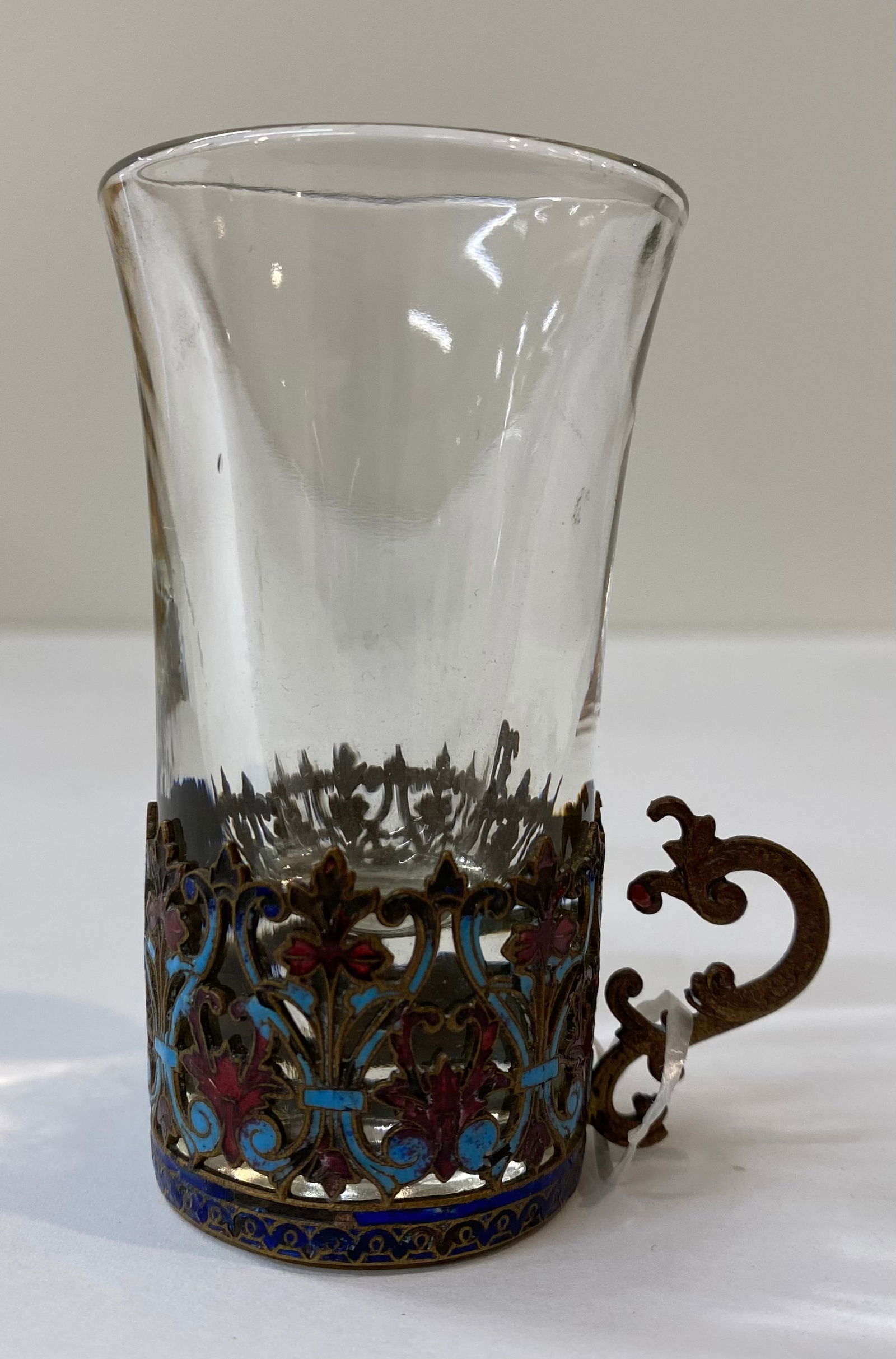 Russian Style Gilt Bronze and Cloisonné Enamel Glass Holder with Insert: An ornate decorative glass holder (Podstakannik) featuring intricate cloisonné enamel work in shades of blue, red, and white. The holder boasts a scrolling "C" curve handle and a crown-motif