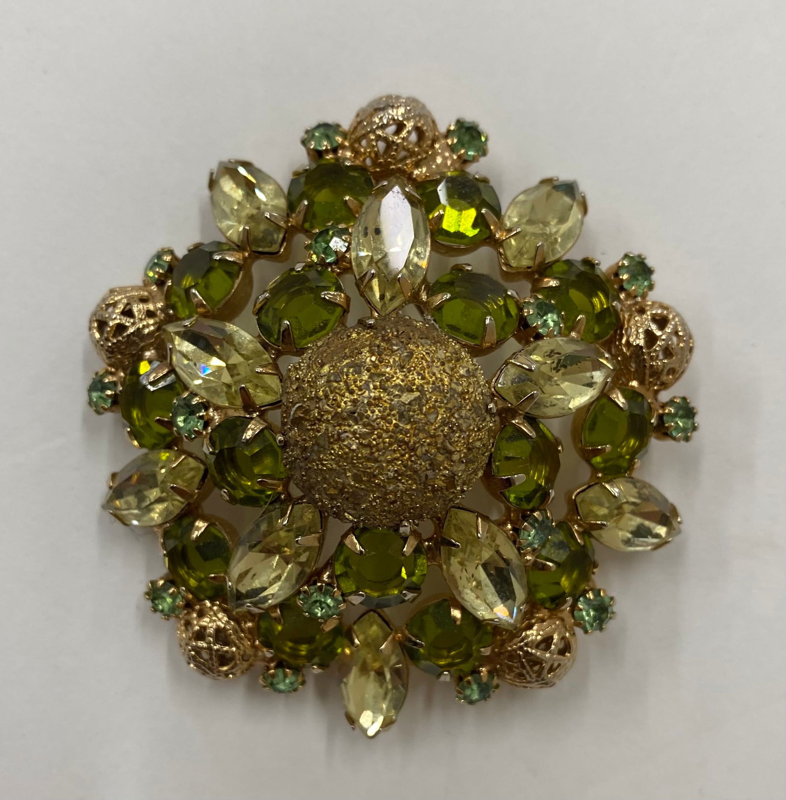 Vintage Juliana Style Gilt Floral Brooch – Peridot and Olive Rhinestones: A layered, high-dome "Easter Egg" style brooch featuring a brilliant arrangement of peridot-colored marquise stones and olive-green rounds. The center is anchored by a large, textured gold-tone "sugar