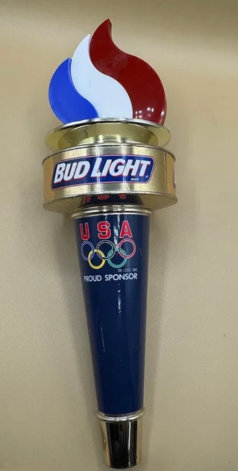 Bud Light Beer Tap Handle USA Olympic Proud Sponsor Torch Red White Blue: A distinctive vintage Bud Light tap handle celebrating their status as a "Proud Sponsor" of the USA Olympic team. This handle is designed in the shape of an Olympic torch, featuring a vibrant red, whi