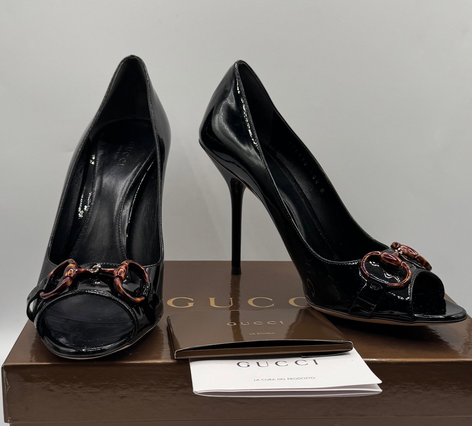 GUCCI Black Patent Leather Peep-Toe Horsebit Pumps: An elegant pair of authentic Gucci peep-toe stiletto pumps, crafted in sleek black patent leather. This timeless silhouette features Gucci’s iconic horsebit accent on the vamp, beautifully