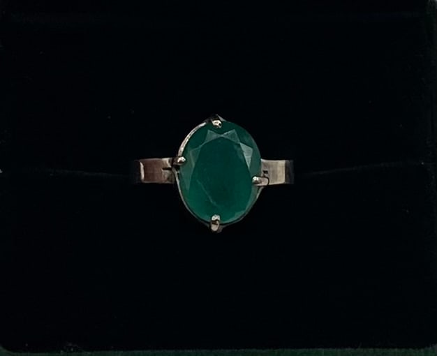 Vintage Emerald Ring: A striking vintage estate statement ring featuring a prominent, oval-faceted deep green emerald gemstone. The stone is securely held in an elevated four-prong collet setting, mounted on a sleek, polis
