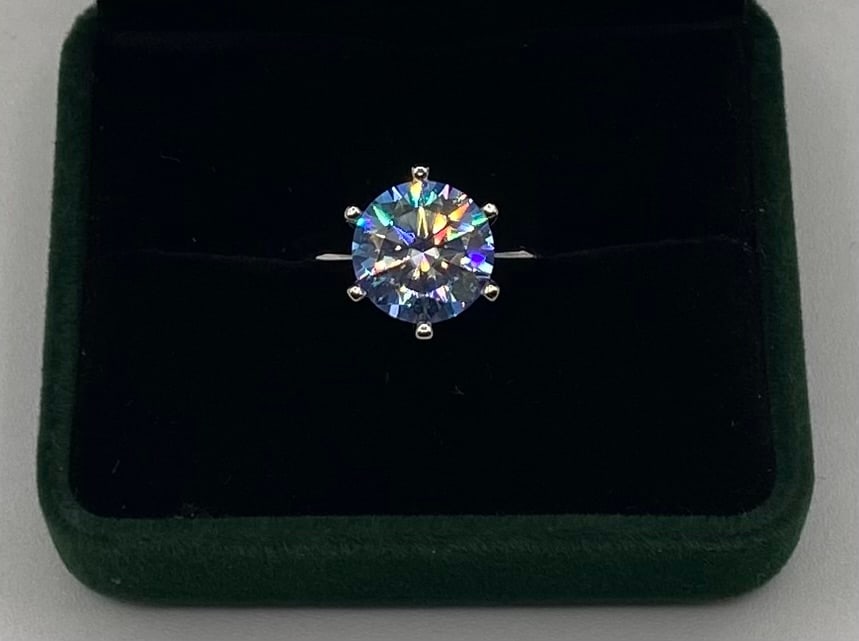 Blue Moissanite Solitaire Ring in 18K White Gold Over Silve: Gemstone: Lab-Created Moissanite Carat Weight: Approx. 5.00 Carat Center Stone Cut: Round Brilliant Cut Metal: 18K White Gold Plated over Solid .925 Sterling Silver Ring Size: 7 Certification:
