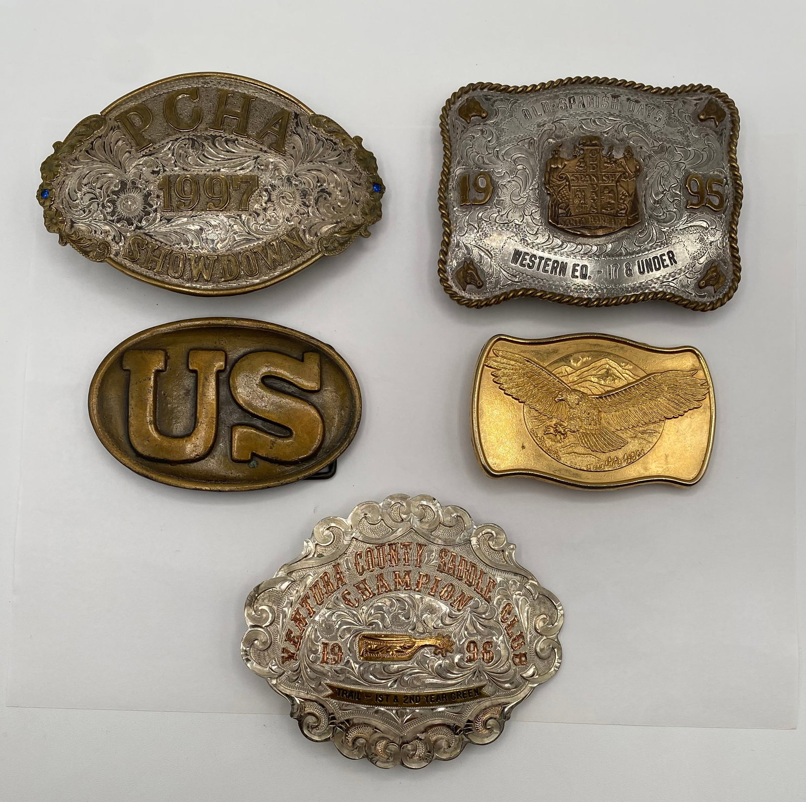 Vintage Western Rodeo & Military Belt Buckle Lot - Silver/Gold Tone, PCHA, US Cavalry: A premium selection of 5 vintage collectible belt buckles, highlighting ornate Western craftsmanship and historical style. Top Left: Large oval PCHA (Pacific Coast Horsepen Association) 1997 Showdown 