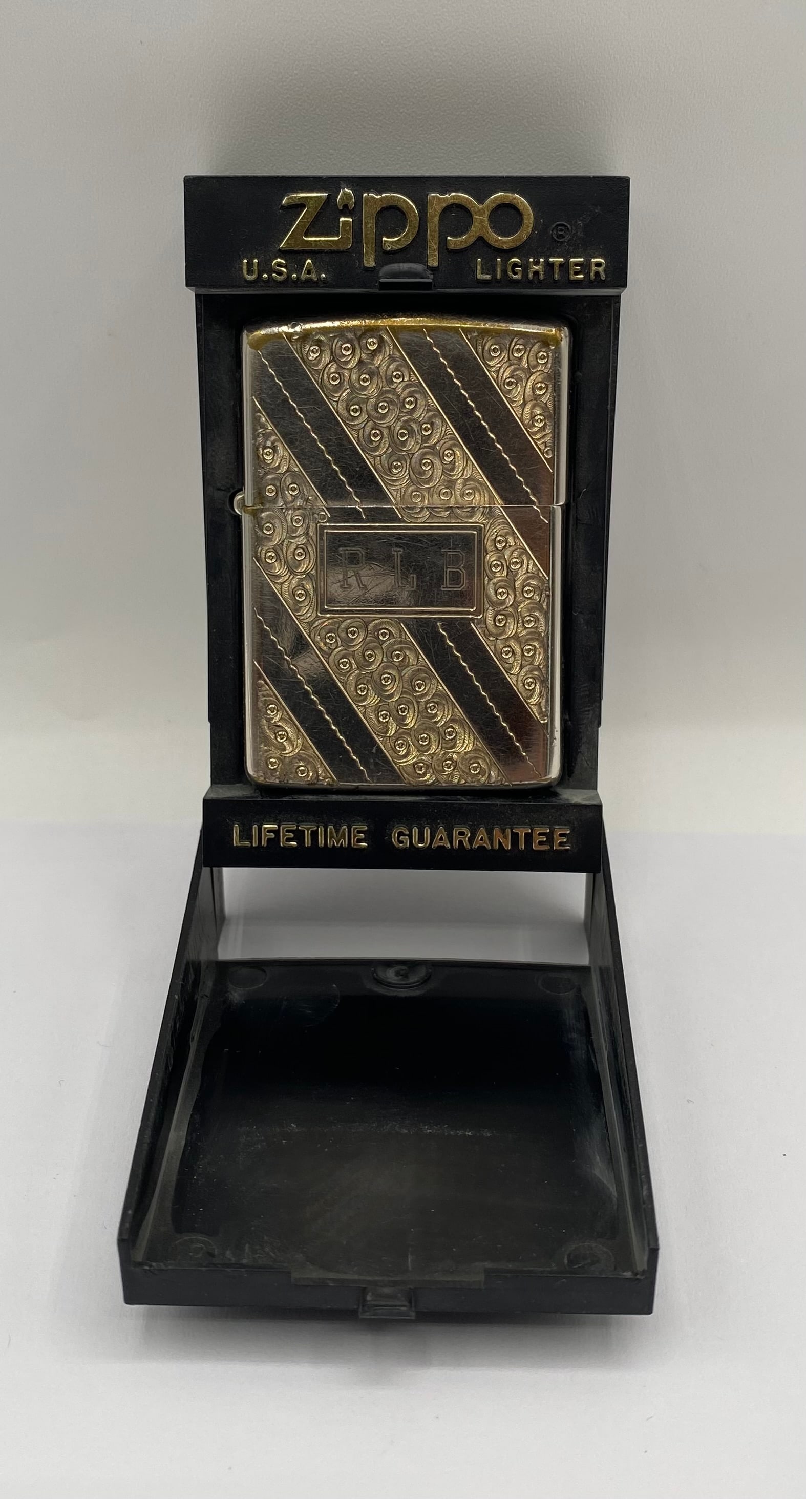 Vintage Monogrammed Zippo Lighter in Original Display Case: A classic vintage Zippo pocket lighter made in the U.S.A. The exterior boasts a polished silver-tone finish with an elegant, deeply engraved diagonal striped and scroll-work pattern. The center