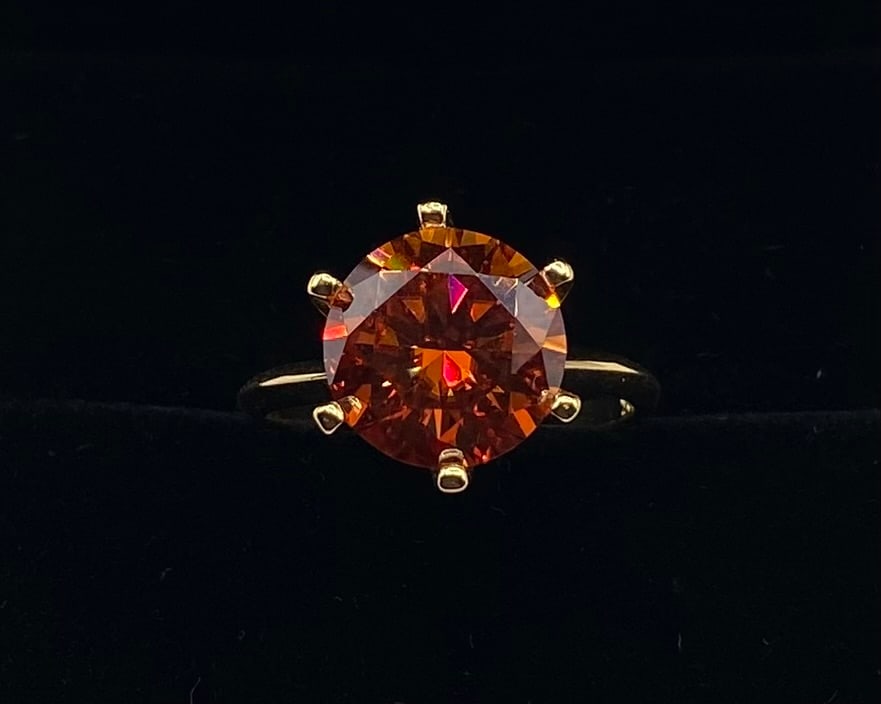 5ct Red VVS1 Moissanite Solitaire Ring w/ Certificate - Size 8: Main Stone: 5.0 Carat, VVS1 Clarity Fancy Cognac / Amber Moissanite Cut: Round Brilliant Cut Setting: Classic 6-Prong Gold-Tone Solitaire Band Ring Size: 8 Includes: Certificate of