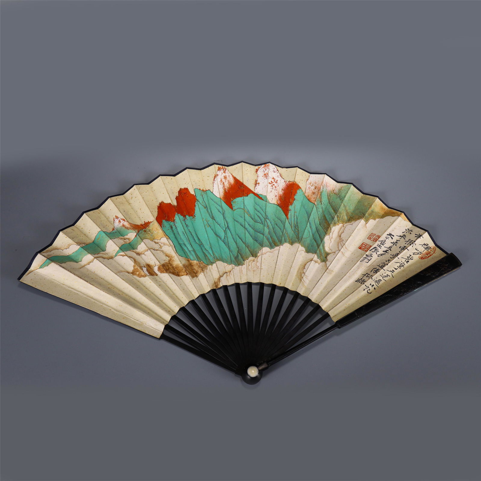 A CHINESE FAN PAINTING OF MOUNTAIN SCENE: A CHINEES FAN PAINTING OF MOUNTAIN SCENE 29.7 cm H x 2.2 cm L x 2.7 cm W x Weight 60 gram. The fan bone is made of hard wood, the fan is divided into two sides, the front is the main painting, and the